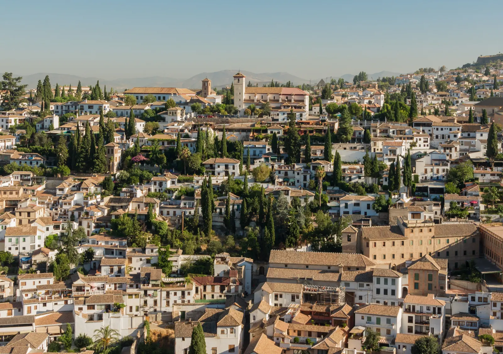 Whitewashed houses and cypress trees climbing the Albaicín hillside in warm evening light